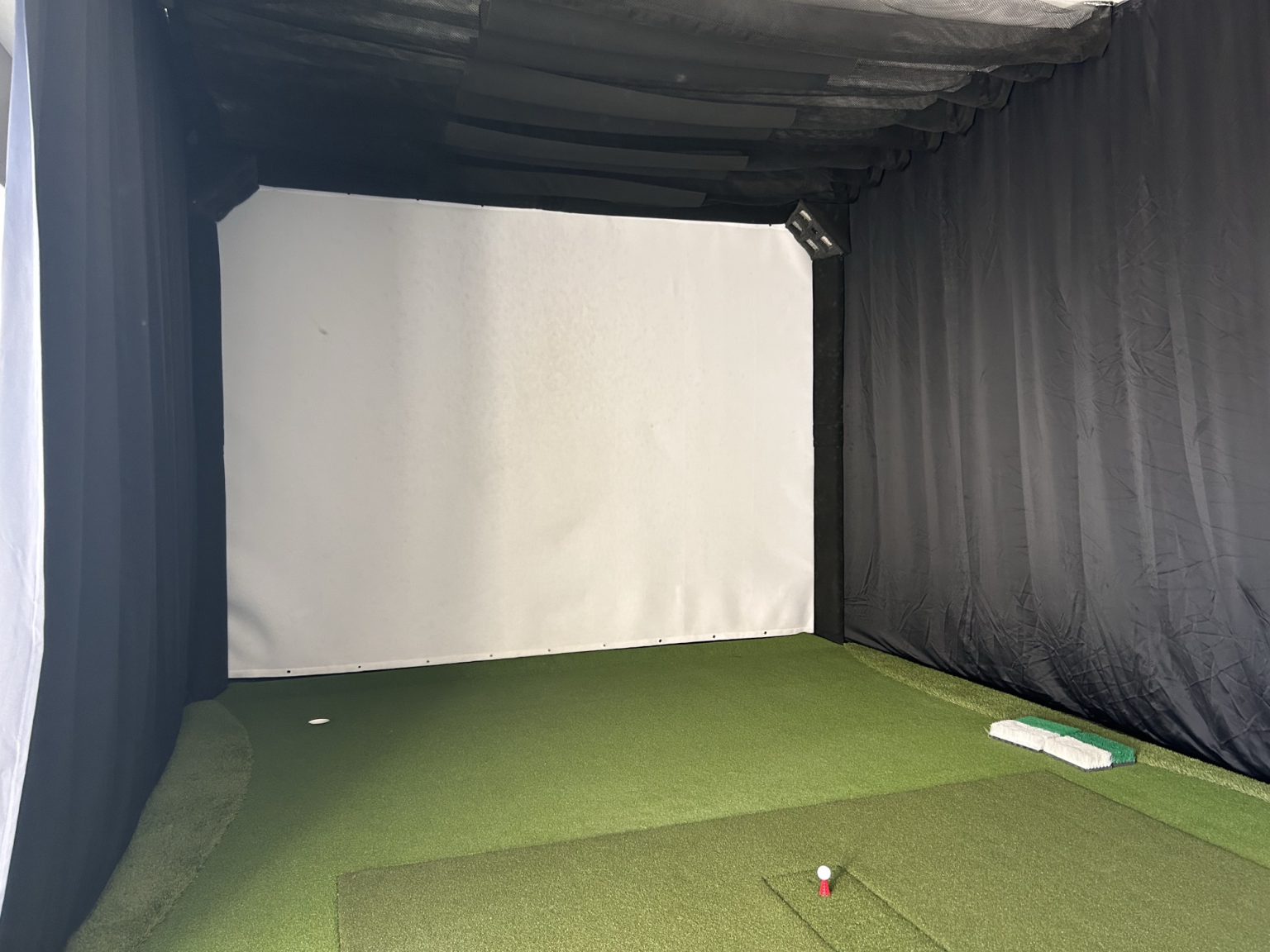 Golf simulator bay with impact screen and hitting mat