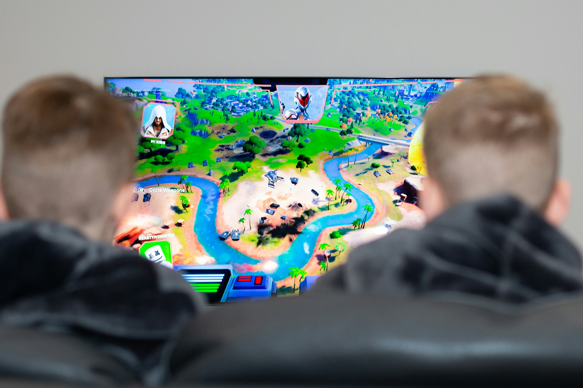 Two friends on a couch playing a video game on a wall-sized screen