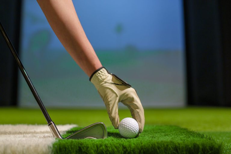 Golfer placing a ball on the hitting mat inside a golf simulator